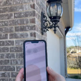 Person holding a smartphone with an app displayed outdoors near a brick wall and lamp post.