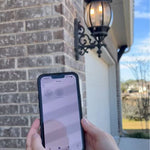 Person holding a smartphone with an app on it in front of a house exterior.
