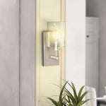 Modern wall sconce with glass shade on a neutral wall with a plant in the foreground.