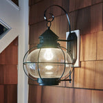 Illuminated outdoor wall lantern with a clear glass globe and dark metal frame mounted on cedar siding